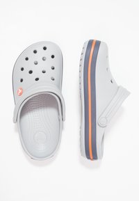 Grå tresko laget av fleksibelt materiale, med ventilasjonshull, hevet hæl og en kontrasterende stripe i oransje og marineblå.