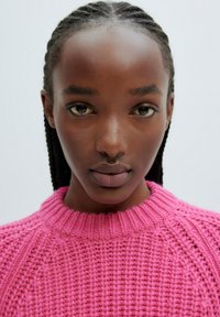 Pull en tricot rose vif avec un col rond côtelé, présentant des détails de couture proéminents et une texture douce.