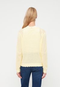 Ανοιχτό κίτρινο πλεκτό πουλόβερ με χαλαρή εφαρμογή, σκαλιστό στρίφωμα και μακριά μανίκια, που διαθέτει ανοιχτό πλέγμα και ριμπ μανσέτες.