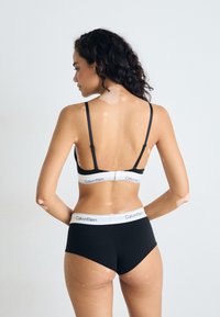Ensemble de lingerie noir Calvin Klein comprenant un bralette avec des fines bretelles et une culotte taille haute assortie, toutes deux avec des ceintures estampillées.