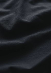 Tejido oscuro y suave con un brillo sutil, que presenta pliegues y arrugas suaves, resaltando su textura y profundidad en el color.