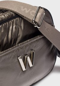 Bolsa gris acolchada con un emblema metálico de "W" y una correa ajustable beige con un hebilla plateada.
