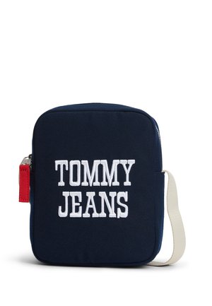 Bolso bandolera cuadrado azul marino con texto blanco "TOMMY JEANS", cremallera roja y correa de hombro ajustable blanca.
