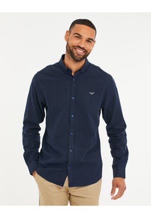 Camisa de botones azul marino hecha de una tela texturizada, con cuello abotonado, botones azules y un pequeño logo bordado en el pecho.