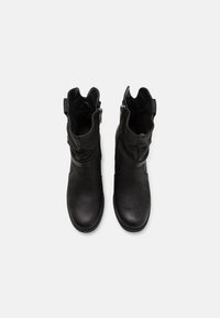 Botas de tobillo negras hechas de cuero texturizado, con suela plana, cremallera lateral y una correa decorativa con acentos cortados.