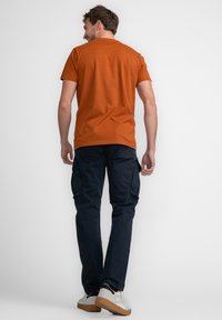 Oranje katoen t-shirt voor heren, gecombineerd met marineblauwe cargo-broeken met zijzakken en een relaxte pasvorm. Witte en beige sneakers.