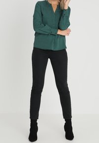 Grön rutigt skjorta med V-ringning, långa ärmar och svarta slim-fit byxor som är matchade med svarta ankelstövlar.