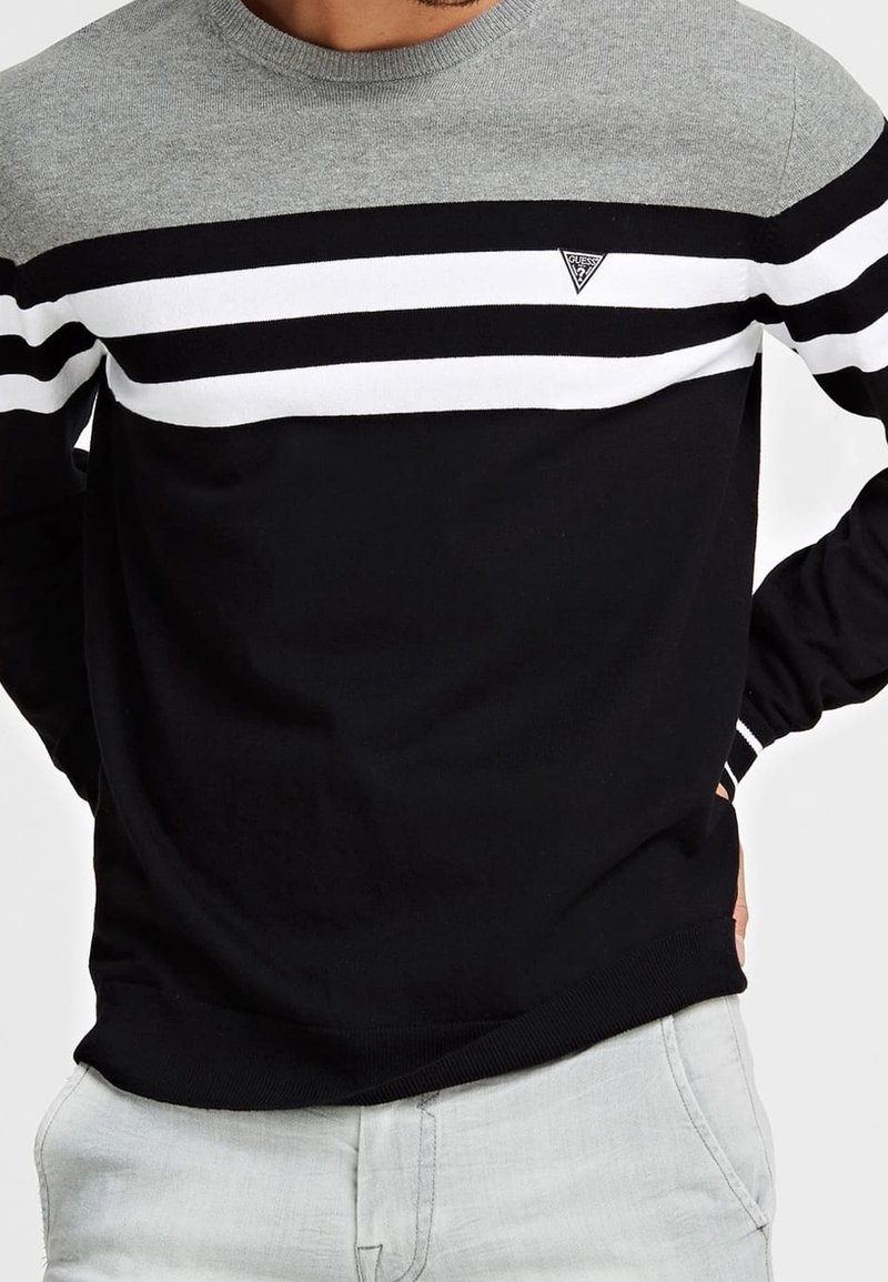 Sweatshirt rayé noir et gris avec un col rond, des rayures horizontales blanches, et un petit logo triangulaire sur le côté gauche de la poitrine. Texture douce.