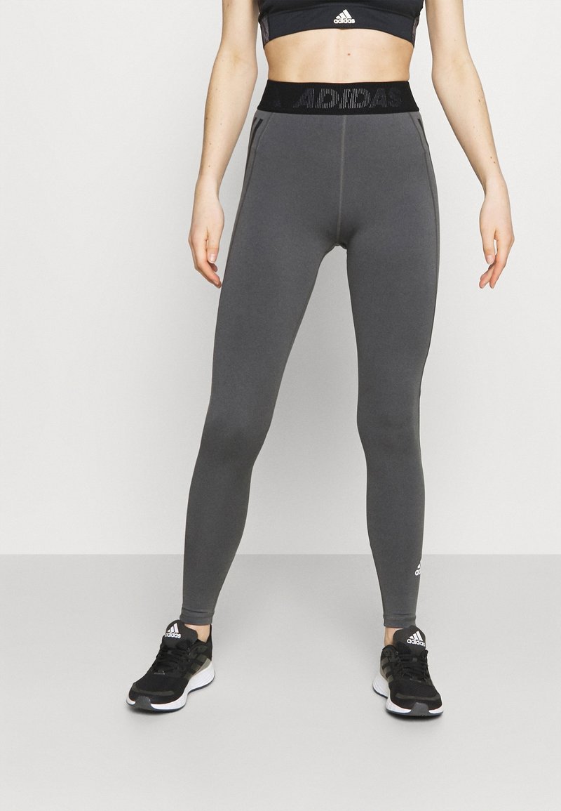 Šedé sportovní legíny s širokým černým pasem, na kterém je logo "ADIDAS", hladký povrch a přiléhavý design pro pohodlí a flexibilitu.