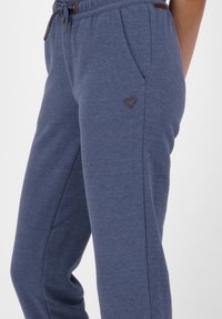 Joggingbyxor, blå melerat tyg, elastisk midja med snörning, sidofickor, diskret brun hjärta-logotyp på höften, avslappnad passform.