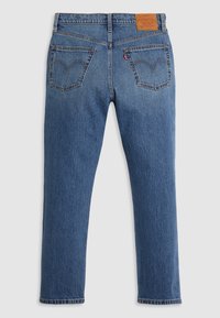 Jean en denim bleu vu de dos avec deux poches, coutures orange, un patch de marque en cuir marron et une étiquette en tissu rouge sur la poche droite.