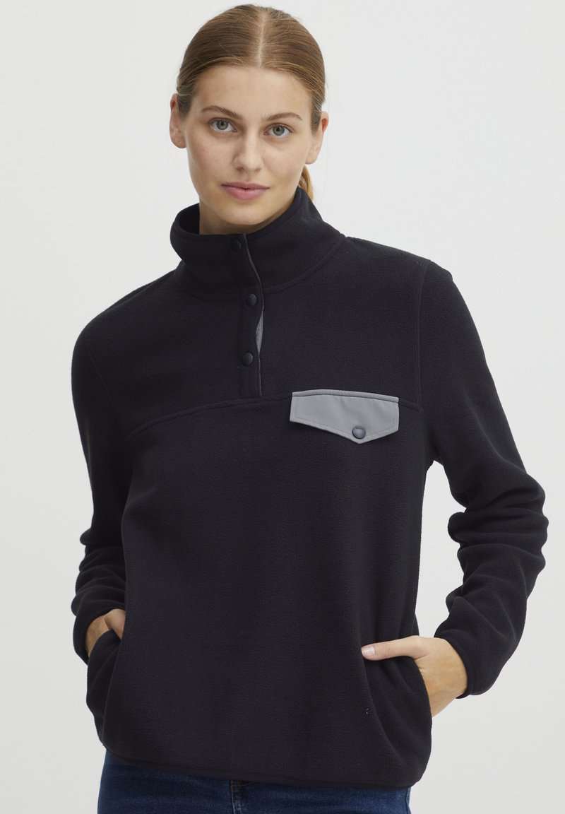 Sort fleece pullover med høj krave, grå brystlomme, tre knapper og sidelommer. Blød tekstur, afslappet pasform og minimalistisk design.