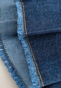 Échantillons de tissu en denim dans différentes nuances de bleu, présentant des bords effilochés et des coutures contrastantes, mettant en valeur différentes textures et motifs.