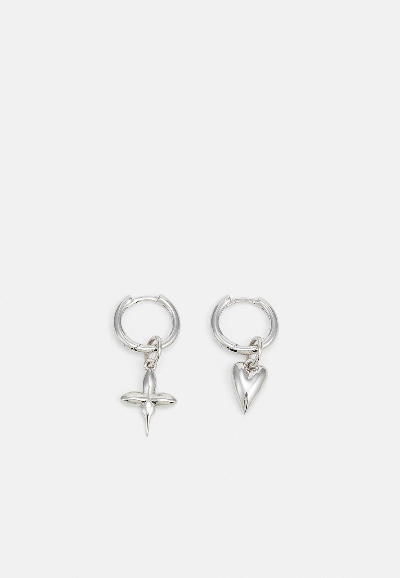 Boucles d'oreilles en argent en forme de cerceau avec un charme croix et cœur. Texture lisse et brillante avec une finition polie. Chaque charmepend d'une boucle sécurisée.