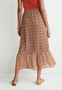 Jupe maxi avec une taille élastique, présentant un motif à carreaux en rouge, marron, olive et crème. Détail de bord à volants.