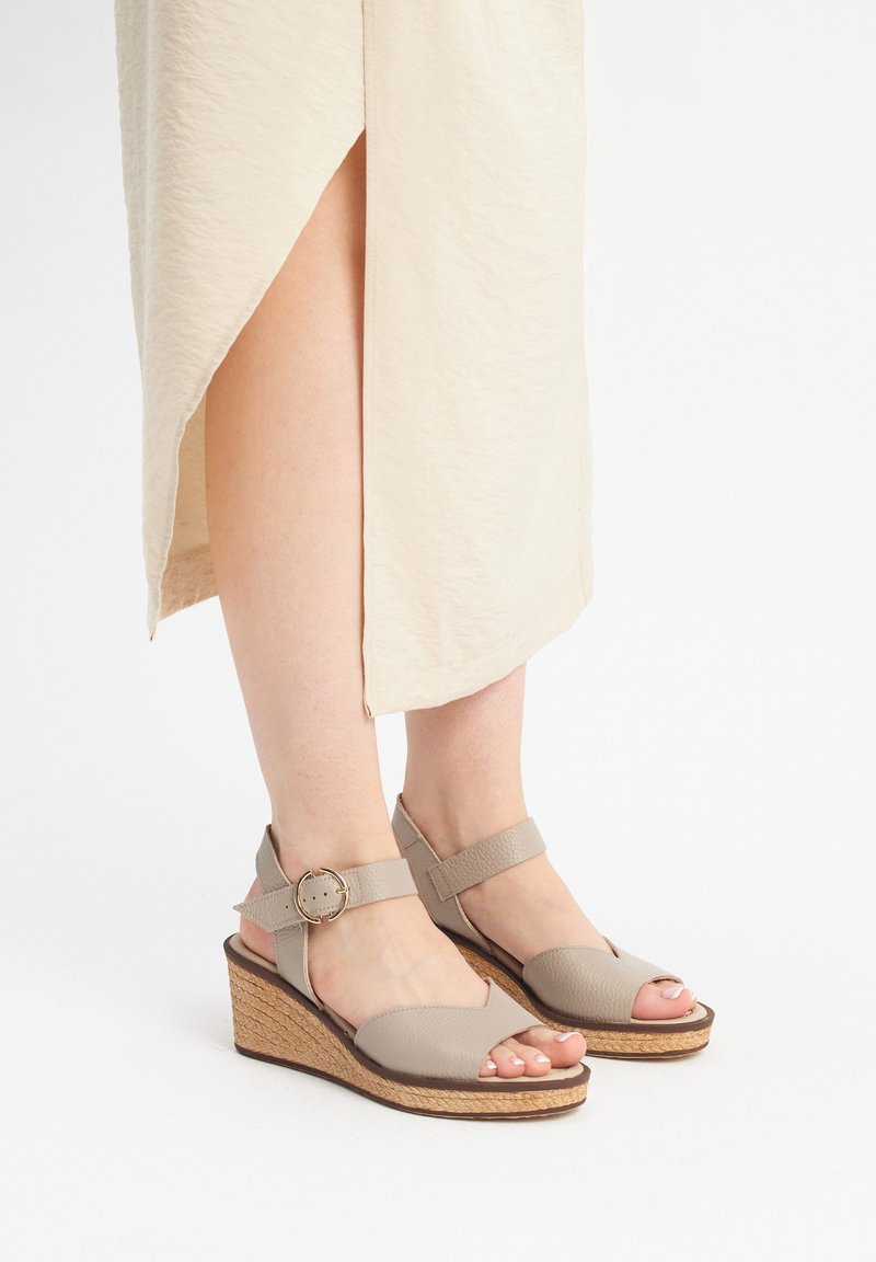Beżowe sandały na koturnie z teksturowanej skóry, z otwartym noskiem i paskiem z klamrą. Podeszwa owinięta juty dodaje naturalnego akcentu.