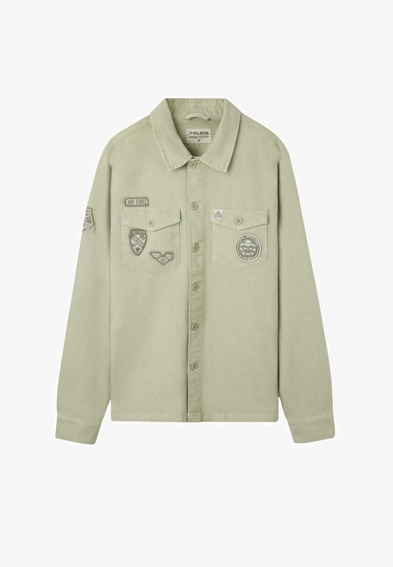 Camisa de botón color khaki claro con mangas largas, dos bolsillos en el pecho y parches y insignias de estilo militar en la parte delantera y en la manga izquierda.