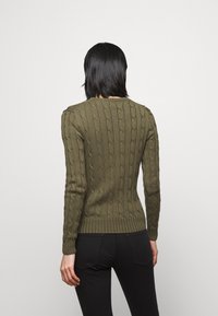 Olivgrön kabelstickad tröja med ribbade muddar och fåll, med rund halsringning och långa ärmar, visad bakifrån.