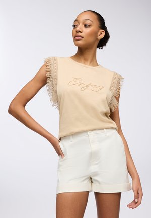 Top in cotone beige senza maniche con dettagli frangiati alle maniche e ricamo "Enjoy". Abbinato a pantaloni corti bianchi con risvolto. Texture morbida.