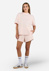 Lyse rosa bomull T-skjorte med avslappet passform, paret med matchende shorts. Hvite joggesko med svarte striper og knelange sokker med tekst.