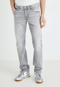 Γκρίζα τζιν παντελόνια με κανονική εφαρμογή, ξεθωριασμένη υφή, πέντε τσέπες και κλείσιμο με κουμπί, συνδυασμένα με μεταλλικά ασημί sneakers.