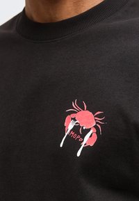 Γραφικά ενός κόκκινου καβουριού με πιρούνι και μαχαίρι σε μαύρο ύφασμα, μερική θέα στον λαιμό και τον ώμο ενός ατόμου.