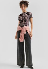 Zwart en roze gestreepte t-shirt met korte mouwen, gecombineerd met hoge zwarte wijde jeans en een roze sweatshirt dat om de taille is geknoopt.
