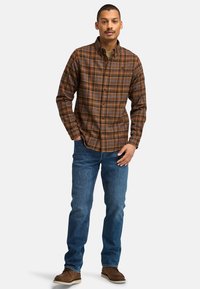 Bruine geruite overhemd met oranje en blauwe accenten, gecombineerd met blauwe spijkerbroek en bruine laarzen; voorzien van een klassieke kraag en een vooraan sluiting met knopen.