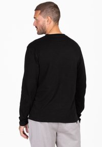 Schwarzes Langarm-T-Shirt aus Baumwolle mit Rundhalsausschnitt. Verfügt über ein einfaches Design, eine taillierte Silhouette und gestickte Akzente am Saum.