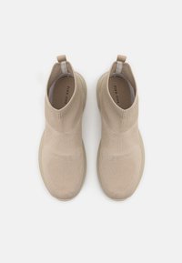 Beige strikkede slip-on sneakers med høy topp-design, teksturert overdel og elastisk krage. Glatt gummisåle med en lys nyanse.