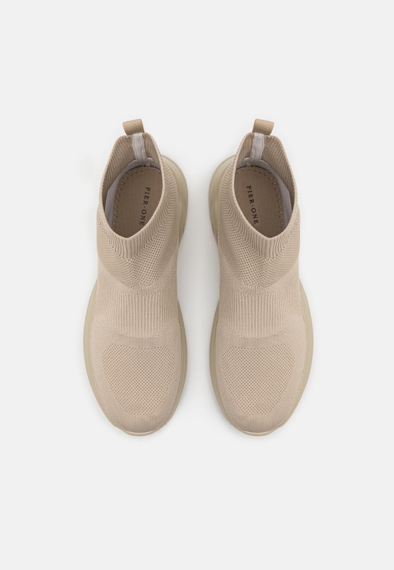 Baskets slip-on en tricot beige avec un design montante, tige texturée et col élastique. Semelle en caoutchouc lisse de teinte claire.