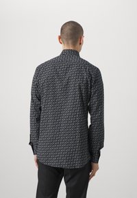 Camicia a maniche lunghe nera e grigia con un motivo geometrico, dotata di colletto alla francese e polsini con bottone. Rifinitura del tessuto liscia.