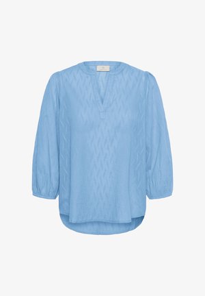 Gaiši zila blūze ar smalku tekstūru, V veida kakla izgriezumu, 3/4 garuma pūkainām piedurknēm ar elastīgiem rokturīšiem un nedaudz izliekts apakšmalu.