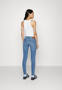 Smala blåjeans med midjeband, två bakfickor och ett brunt logopatch. Bärs med en vit ärmlös topp och sneakers med blå accenter.