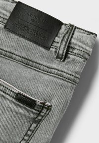 Grå denimjeans har en svart läderlapp i midjan, kontrasterande sömmar och en klassisk femficksdesign.