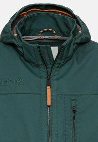 Mørkegrøn jakke med lynlåslukning foran, tekstureret stof og orange detaljer indeni hætten. Har en lille brystlomme.