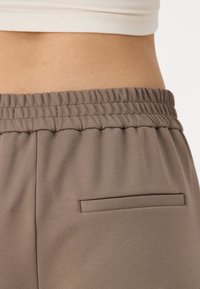 Ljusbruna, mjuka tygbyxor med resårmidja och en liten, smal bakficka. Slät textur, figurnära design runt midjan.