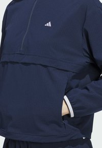 Navy blue zip-up pullover made of ribbed fabric, featuring a high collar, white accents, and a small logo on the chest.