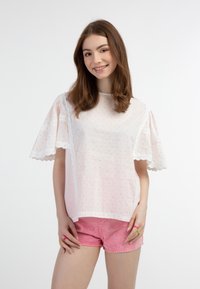 Blusa bianca a maniche corte con pois rosa, bordo in pizzo sulle spalle, abbinata a pantaloni corti rosa chiaro. Texture liscia, design casual.