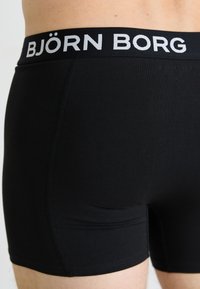Nahaufnahme einer Person, die schwarze Björn Borg Boxershorts mit sichtbarem Logo-Bund trägt.
