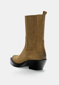 Botte en daim marron mi-mollet avec un talon empilé noir, un panneau latéral élastique et une languette sur un fond neutre.