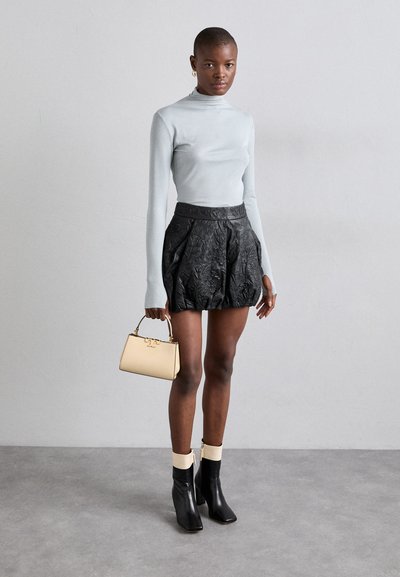 Pull col roulé ajusté bleu clair, mini-jupe noire à motifs floraux en relief, sac à main beige et bottines noires avec des revers crème. Accessoires simples.