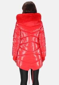 Piros puffadt dzseki fényes felülettel, szőrmebéléses kapucnival és bordázott mandzsettákkal. Chevron steppeléssel és állítható zsinórral a szegélyén.