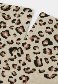 Stickade strumpor i leopardmönster i beige med svarta och bruna fläckar, med ribbad textur och rullad fåll.