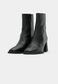 Botas de cuero negro hasta el tobillo con un acabado suave, punta cuadrada, cremallera lateral y un tacón ancho. Diseño sencillo y contemporáneo.