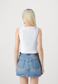 Biely rebrovaný bezrukávový crop top v kombinácii s modrou džínsovou sukňou. Sukňa má roztrhnuté okraje a zadné vrecká.