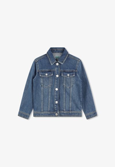 Veste en denim avec un délavage bleu classique, deux poches poitrine et des boutons argentés. Elle possède un col structuré et des détails de couture visibles.