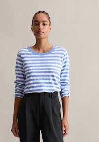 Długi rękaw, w paski, top w jasnoniebieskim i białym kolorze z okrągłym dekoltem, w połączeniu z czarnymi spodniami o wysokim stanie.