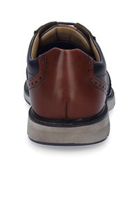 Lederschuh mit einem navyblauen Obermaterial und einer braunen Ferse. Verfügt über Broguemuster, eine Gummisohle und beiges Futter, das von der Ferse aus sichtbar ist.