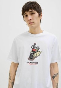 Tricou alb din bumbac cu un grafic reprezentând un schelet pe o motocicletă, cu textul "JACK&JONES Originals" în negru și roșu sub design.